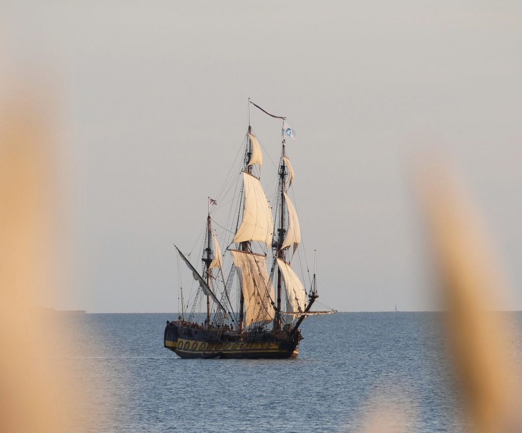 Äldre segelfartyg med vita segel ute på havet.